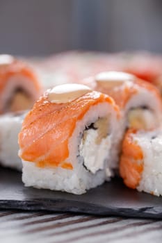 Popular food. Set of Philadelphia sushi on black concrete plate on table. Close up of pieces of sushi rolls with salmon on top and with cheese and eel inside.