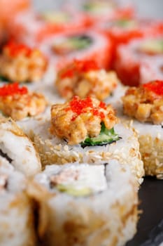 Traditional japanese sushi roll with tuna, tobiko red caviar and cucumber. Close up of piece of sushi covered with white sesame seeds and topped with minced tuna and red caviar and covering filling.
