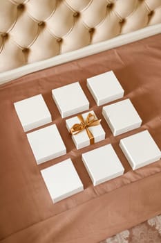 Presents for holidays. Set of small minimalist gift boxes for jewelry spread out on luxury bed. Close up of nine white square boxes one of which is tied with brown ribbon.