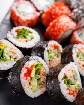 Asian cuisine. Large sushi set of various sushi rolls is served on black square metal slate. Side view of different rolls with variety of fresh ingredients.