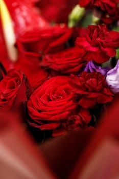 Beautiful large bouquet composed of red and purple flowers. Bouquet of roses, calla lilies and eustoma wrapped in red floral film and tied with purple satin ribbon closeup view
