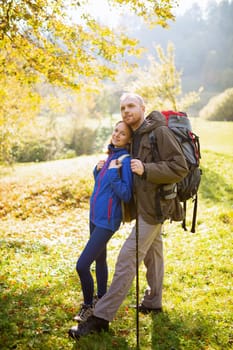 Portrait of a young couple in love traveling together in the mountains and standing hugging on top of a hill. Man and woman hikers enjoy the beauty of nature together. Travel and lifestyle concept.