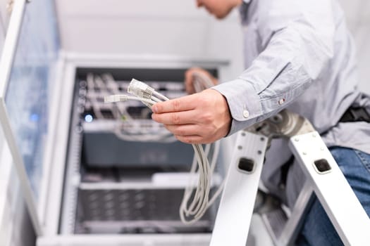 Internet network connection. Male technician's hand holds group of white network cables before connecting to port switch. Close up of plugs for internet connection in hands of man standing on ladder.