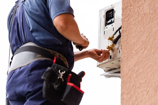 Professional male technician repairing modern air conditioner outdoors. Close up of man checking, repairing or installing outdoor air conditioner unit hanging a wall outside. Selective focus.