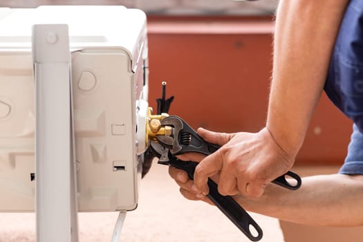 Man holds wrench in his hand. Male technician using spanner when installing modern air conditioning system. Worker on street installs outdoor air conditioner unit. Close up. Selective focus.