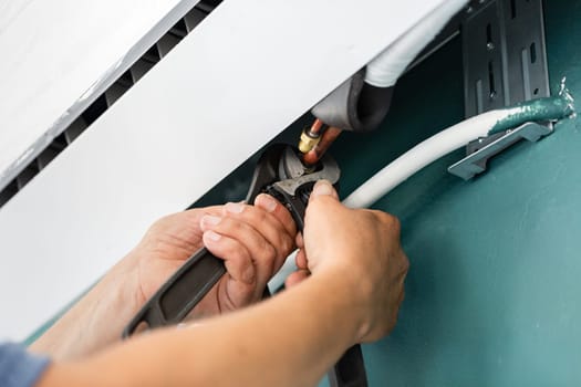 Mechanic and repairman. Professional male technician works on installation of air conditioners. Close up of hands of male worker who uses metal fixed wrench to tighten outdoor unit of air conditioner.