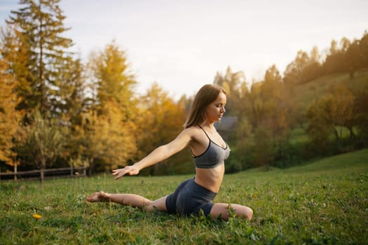 Yoga outdoor. Woman practices yoga exercises, meditation and stretching on the grass among the mountain autumn nature. Concept of healthy lifestyle and relaxation.