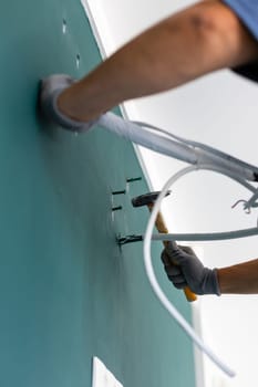Close up of hammering nail in wall. Male worker drives dowels into wall before installing air conditioner. Bottom view at angle of hands holding hammer and cords from air conditioning system.
