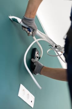 Measuring at construction site. Handyman makes wiring and installs air conditioning during repairs in new apartment. Close up of worker attaching modern digital measuring device to wall.