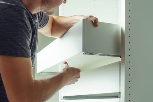 Male hold drawer, inserting and securing it to rails, assembling white dresser or wardrobe. Self-assembly of furniture at home, DIY, furniture repair and rearrangement