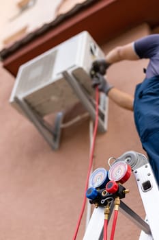 Worker maintains outdoor air conditioner using manometers for filling air conditioners. Equipment for filling home air conditioner after cleaners and checking maintenance outdoor air compressor unit.