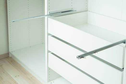 Drawer rail inserted into cabinet, fixed with self-tapping screws. Assembling white dresser or wardrobe. Self-assembly of furniture at home, DIY, furniture repair and rearrangement