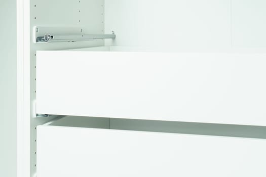 Drawer rail inserted into cabinet, fixed with self-tapping screws. Assembling white dresser or wardrobe. Self-assembly of furniture at home, DIY, furniture repair and rearrangement