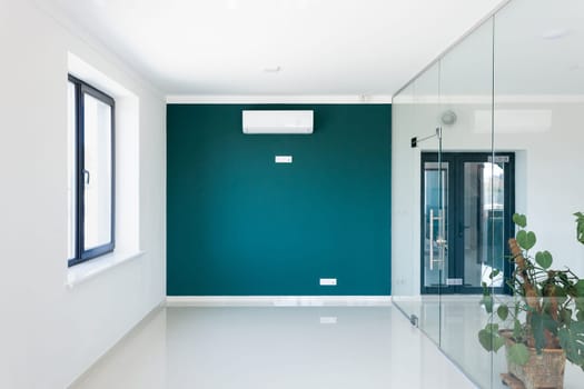 Stylish empty office interior with air conditioning on wall in modern business center. Green wall with air conditioning and sockets, white walls and glass doors in modern office space.