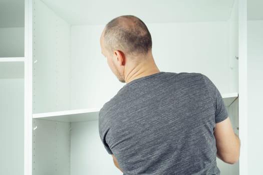 Male hold shelf, inserting and securing it to supports, assembling white dresser or wardrobe. Self-assembly of furniture at home, DIY, furniture repair and rearrangement