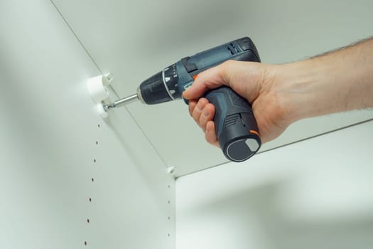 Male hands screw in to insert plastic support into one of series of holes to fix white hanger bar, assembling dresser or wardrobe. Holds screwdriver. Self-assembly of furniture, DIY, renovation