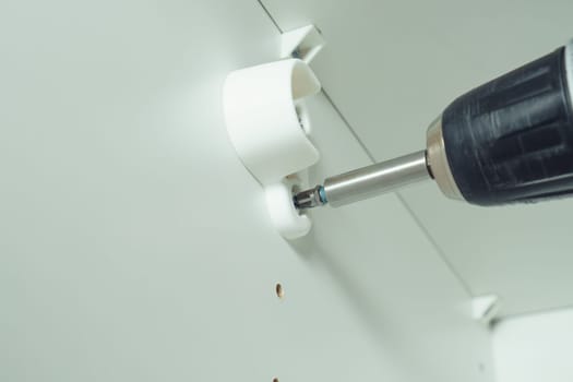 Closeup of screw in to insert plastic support into one of series of holes to fix white hanger bar, assembling dresser or wardrobe. Screwdriver. Self-assembly of furniture, DIY, renovation