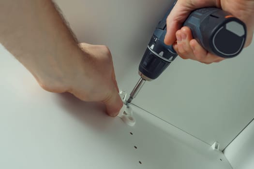 Male hands screw in to insert plastic support into one of series of holes to fix white hanger bar, assembling dresser or wardrobe. Holds screwdriver. Self-assembly of furniture, DIY, renovation