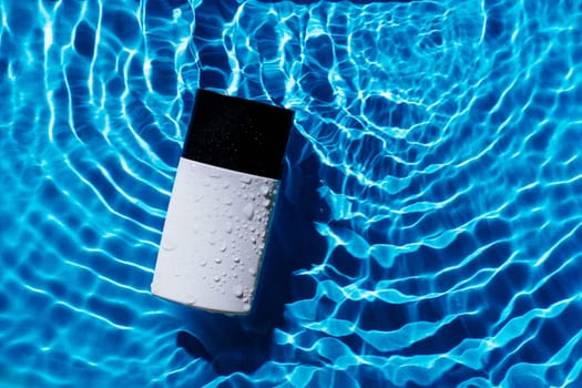 Fashion trendy bottle of perfume toilet water, lotion on blue wave splash background. Advertising beauty cosmetology product. Black and white container making tides. Elegant luxury scent. Copy space