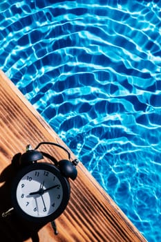 Wood board black alarm daily clock. Blue transparent reflect wave water surface ocean. Time aging running out. Vacation summer health care concept. Countdown youth. Flat lay, place for text. Vertical