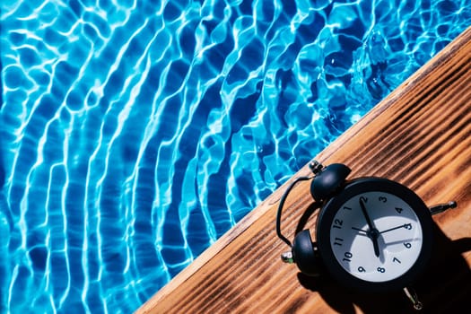 Wood sand board black alarm daily clock. Blue transparent reflect wave water surface ocean. Time aging running out. Vacation summer health care concept. Countdown youth. Flat lay, place for text.