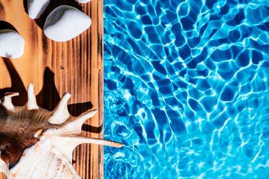 Wood sand board, hot white salt stones and natural seashell, conch. Blue transparent reflect wave water surface ocean. Hot warm stone massage therapy treatment concept. Flat lay. Right place for text.