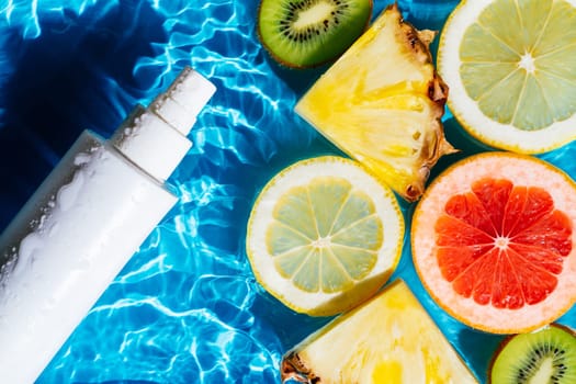 White beauty product sunscreen cream vial sprayer in transparent water with flecks and waves, fruit citrus lemon, kiwi, orange, pineapple, grapefruit. Body skin care protection beach concept. Flat lay