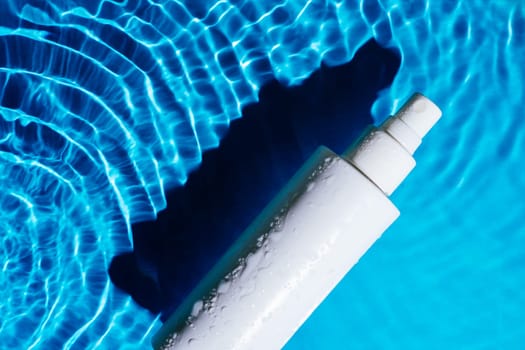 White cosmetic product moisture balm atomizer with pump vial sprayer in transparent fresh blue water with flecks, waves, shade. Body skin care protection in summer beach vacation concept. Flat lay.