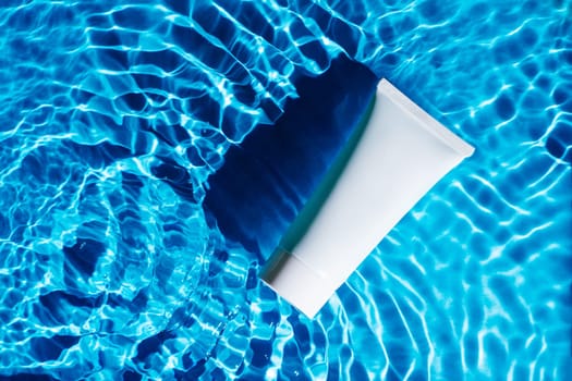 White beauty product sunscreen cream vial tube bottle in transparent fresh water with flecks and waves, dark shade. Body skin care protection in hot summer beach. Flat lay.