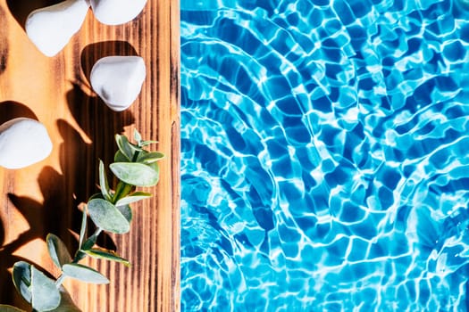 Wood sand board with hot white salt stones and twig natural eucalyptus. Blue transparent reflect wave water surface ocean. Hot warm stone massage therapy treatment concept. Right place for text.