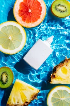 Vertical beauty sunscreen cream vial tube bottle near fruit citrus lemon, kiwi, orange, pineapple, grapefruit, lemon in water. Flat lay, top view. Summer beach body skin care radiation concept