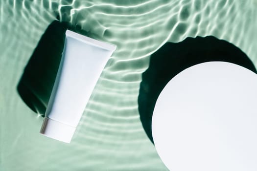 White circle copy space with beauty product sunscreen cream vial tube in transparent green blue water drop splashing surface with flecks, waves, shade. Health care concept. Flat lay. Place for text