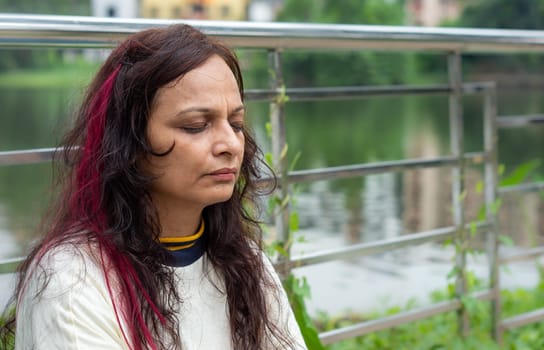 Senior Woman in meditation sitting with eyes closed concentrate in a public park. Side view. Medium Shot. Close up portrait.