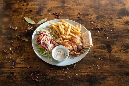 Kebab plate with french frizes and white sauce on a wooden table