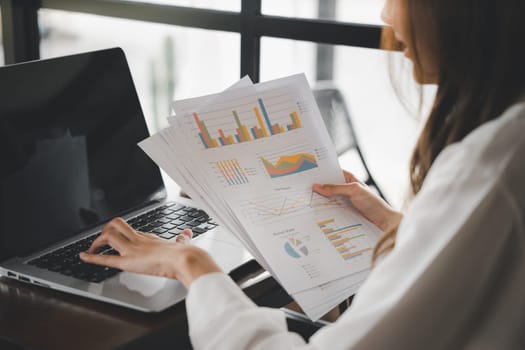 Businesswoman working and comparing forecasting and graphic documents paperwork with laptop computer, Happy female holding papers review report analyzing work results on graph chart outside office