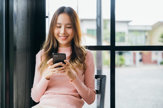 Happy beautiful female typing text message on smart phone device and enjoyment lifestyle with social networking media, Asian young woman using mobile phone at cafe coffee shop to shopping online