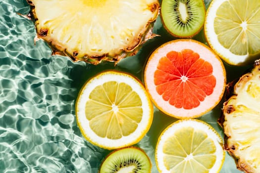 Colorful abstract image fruit citrus lemon, kiwi, orange, pineapple, grapefruit, lemon, pomelo water splashing fresh transparent surface, flecks. Flat lay, top view. Copy space. Summer beach tropical