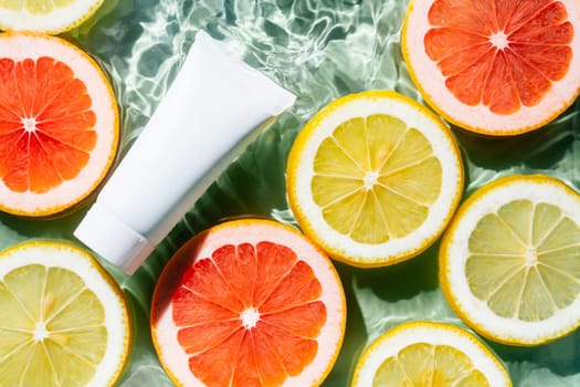 White beauty product sunscreen cream vial tube bottle with fruit citrus lemon and grapefruit slices in water splashing fresh transparent, fleck. Flat lay, top view. Beach tropical. Skin care in summer