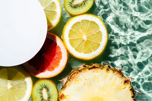White circle copy space with fruit citrus lemon, kiwi, orange, pineapple, grapefruit, lemon, pomelo water splashing fresh transparent surface, flecks. Summer food beach travel drinks concept. Flat lay