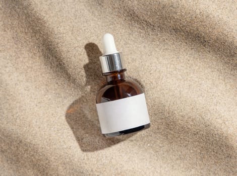 Dropper bottle with blank label on beige sand top view, hard light. Package mockup. Natural skincare product. Facial cosmetics for beauty routine. Zen style with waves on sand, minimal aesthetic