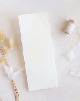 Blank card near silk ribbons and dried hare's tail grass top view on white, mockup. Boho romantic scene with vertical card. Bohemian or close to nature greeting or wedding Invitation