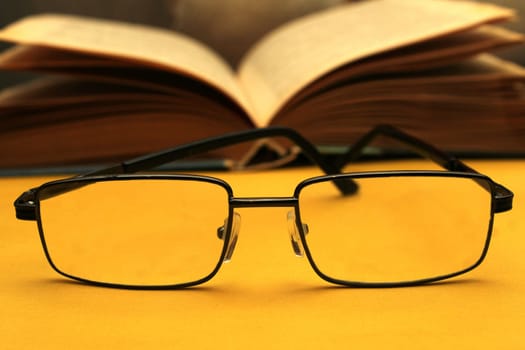 Glasses in a black frame on a yellow background. In the background is an open book. World Day of Sight.