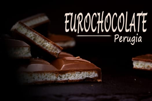 Pieces of milk aerated chocolate close-up on a dark background with an inscription. The concept of the Perugia Chocolate Festival.