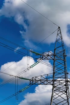 High-voltage power transmission tower with wires. High voltage line. Energy industry. Energy transfer. Blue sky. White clouds. Agricultural field. Cloudy horizon. Business. Electrician work.