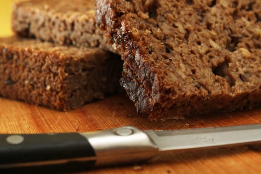 Sliced whole grain bread with a knife on a wooden board. Defocus. Healthy food concept.