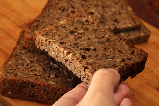 Woman's hand taking whole grain bread, close-up. Defocus. Healthy food concept.