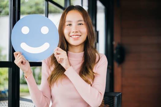 Customer experience review. Happy excited young woman smiling showing excellent rating with smiley face icon on blue circle paper in cafe feedback good service, holding smile emoji, Compliment day