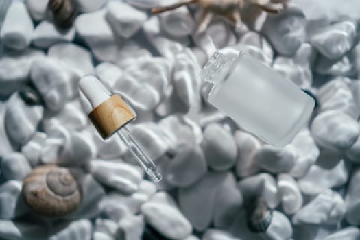 Facial pipette serum oil, essence cosmetic product in bottle on transparent fresh water with fleck and waves, bottom of white stones and shells. Organic skin body antiage care in hot climate. Top view