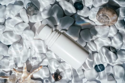 White beauty product roll on antiperspirant deodorant anti sweat smell, vial in transparent fresh water with flecks and waves above bottom of white stones and shell. Skin care protection. Flat lay.