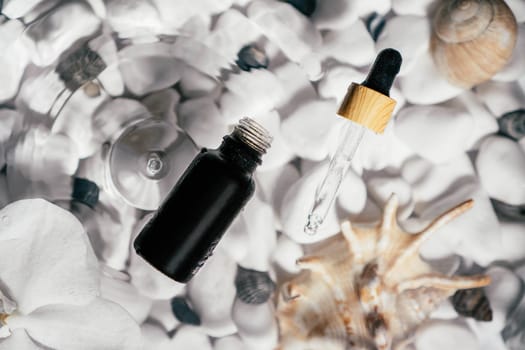 Facial pipette serum oil, essence cosmetic product in bottle on transparent fresh water with fleck and waves, bottom of white stones and shells. Organic skin body antiage care in hot climate. Top view